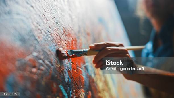 Female Artist Works On Abstract Oil Painting Moving Paint Brush Energetically She Creates Modern Masterpiece Dark Creative Studio Where Large Canvas Stands On Easel Illuminated Low Angle Closeup Stock Photo - Download Image Now
