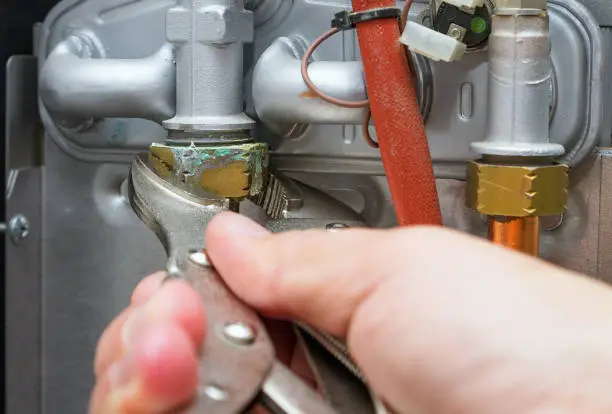 Photo of Servicing a heating home system.Technician with wrench repairs leaked hot water pipe in gas boiler. Close-up, selective focus.