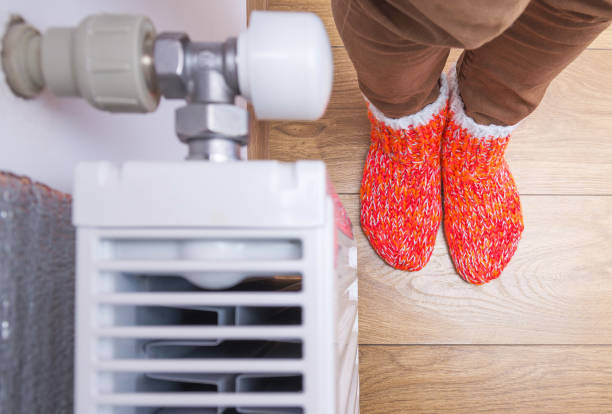 A woman in orange warm winter socks stands near a home heating radiator. Electric or gas heater at home. The symbolic image of the heating season at home. Selective focus. A woman in bright warm winter socks stands near a home heating radiator. Electric or gas heater at home. The symbolic image of the heating season at home. Selective focus. heating oil photos stock pictures, royalty-free photos & images
