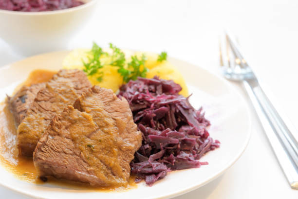 istock braised beef with potatoes, red cabbage and parsley garnish, served on a plate on a white table, copy space 1183190938