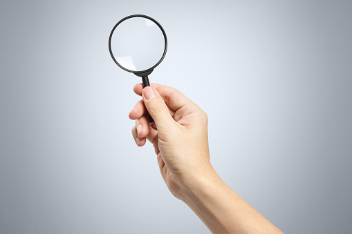 Hand holding a magnifying glass on gray background