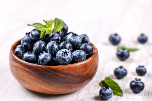 istock Fresh blueberries with green mint leaf in a wooden bowl on white table 1183197604