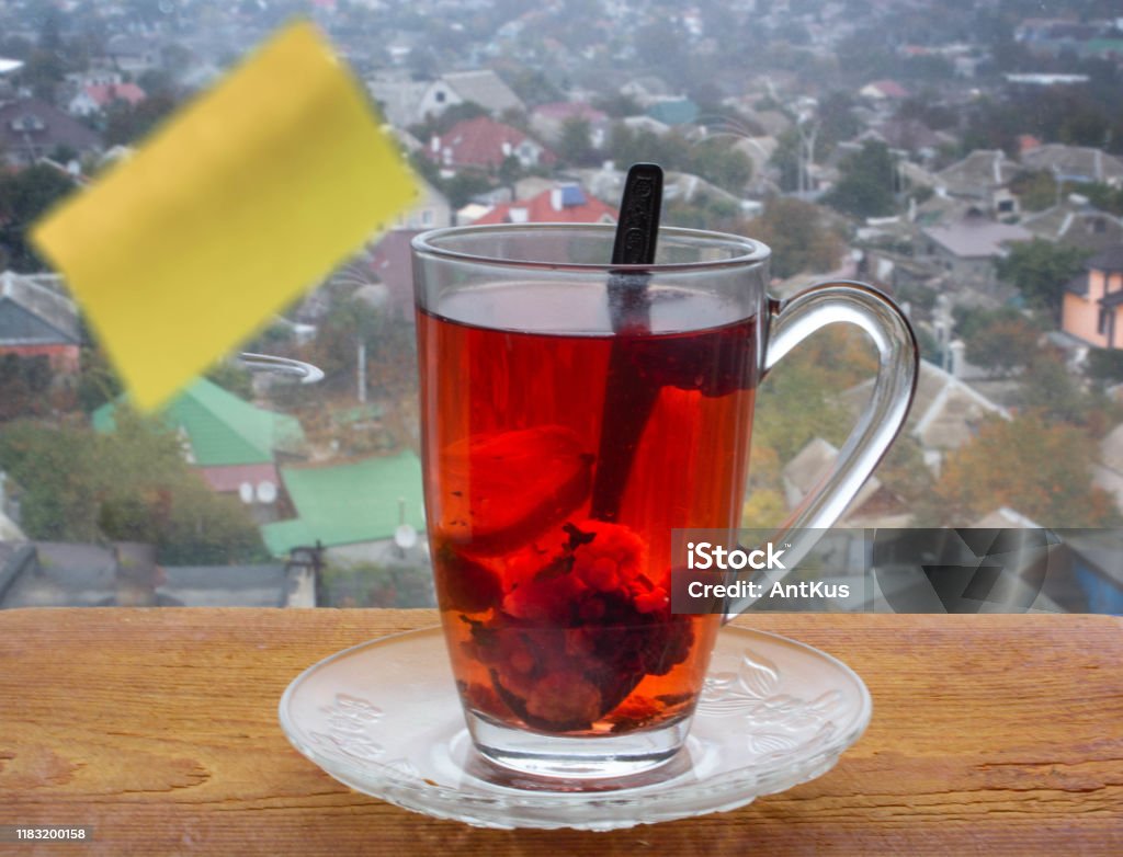 Good morning Red tea with fruits and lemon on a wooden board. A large yellow sticker for notes is glued on the glass. Behind glass a blurred urban background. Alternative Medicine Stock Photo
