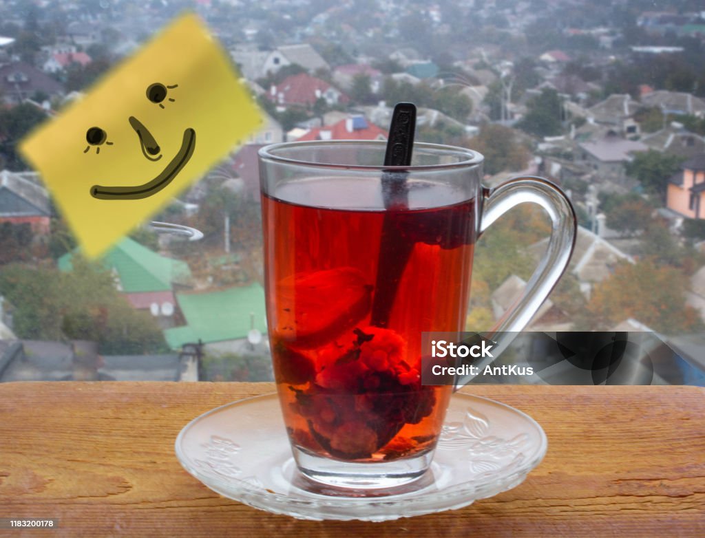 A good day A smile is painted on a yellow sticker. Red tea with fruits and lemon on a wooden board. Behind glass a blurred urban background. Concept of a good start to the day. Alternative Medicine Stock Photo
