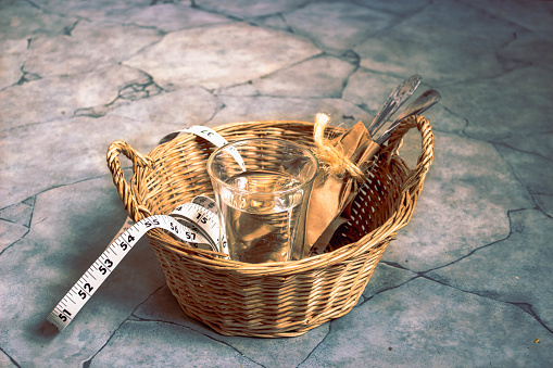 In a wicker brown basket for food there is only a glass with water, a centimeter tape and sheathed cutlery. The concept of a strict diet, hunger strike.