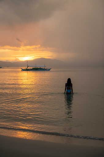 A Filipino woman walks into the sea at sunset in Port Barton, Palawan, Philippines
