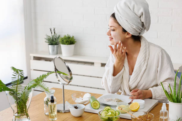 Young woman applying face mask at home. Natural Skin Care Routine For Glowing Skin. Young woman cleaning face with natural cosmetics. How to get clear and glowing skin. Portrait of young woman with clay face mask on wearing bathrobe. Homemade Face Mask homemade stock pictures, royalty-free photos & images
