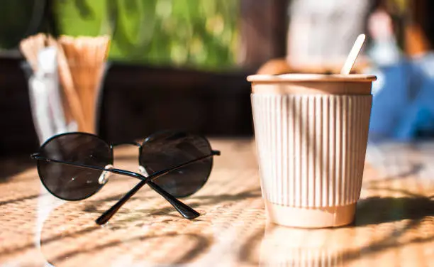 Disposable paper coffee cup with holder on table in cafe with wooden stirrer,near sunglasses.Environmentally friendly lifestyle.Zero Waste,Save The Planet,Earth Day,No Plastic,Recycling Concept