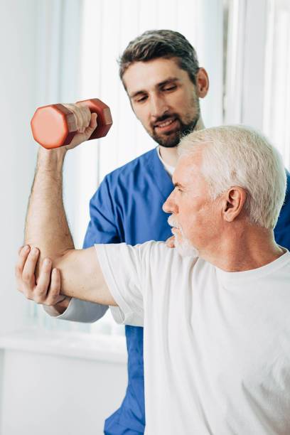 istock senior man lift a dumbbell, he doing treatment exercise with his physiotherapist. Physio treatment at rehab center 1183219038