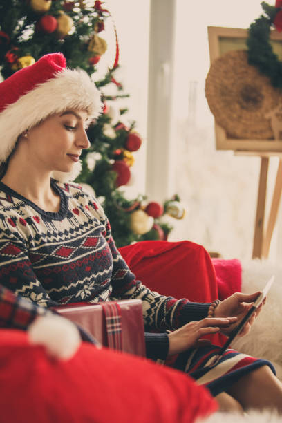 istock Young woman using tablet while relaxing by the Christmas tree 1183219489