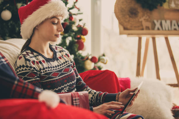 istock Young woman using tablet while relaxing by the Christmas tree 1183219496