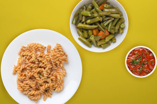 pasta on a white plate in tomato sauce with vegetable salad on a yellow background. Mediterranean cuisine top view. healthy food. flat lay
