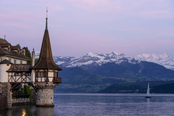 nightscape do castelo de oberhofen que olha para fora lago thun e iluminado no crepúsculo. montanhas cobertas de neve e céu pitoresco no fundo. cantão de berna. - lake thun switzerland night lake - fotografias e filmes do acervo