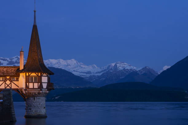 nightscape do castelo de oberhofen que olha para fora lago thun e iluminado no crepúsculo. montanhas cobertas de neve e céu pitoresco no fundo. cantão de berna. - lake thun switzerland night lake - fotografias e filmes do acervo