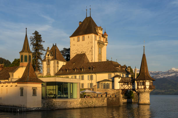 castelo de oberhoffen que olha para fora o lago thun no por do sol. montanhas cobertas de neve e céu pitoresco no fundo. cantão de berna. - lake thun switzerland night lake - fotografias e filmes do acervo