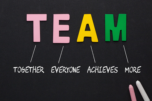 TEAM (Together, Everyone, Achieves, More) text spelled with alphabet letters on black background. Acronym business concept.