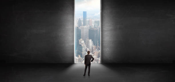 istock Businessman looking to a cityscape from a dark empty room 1183227541