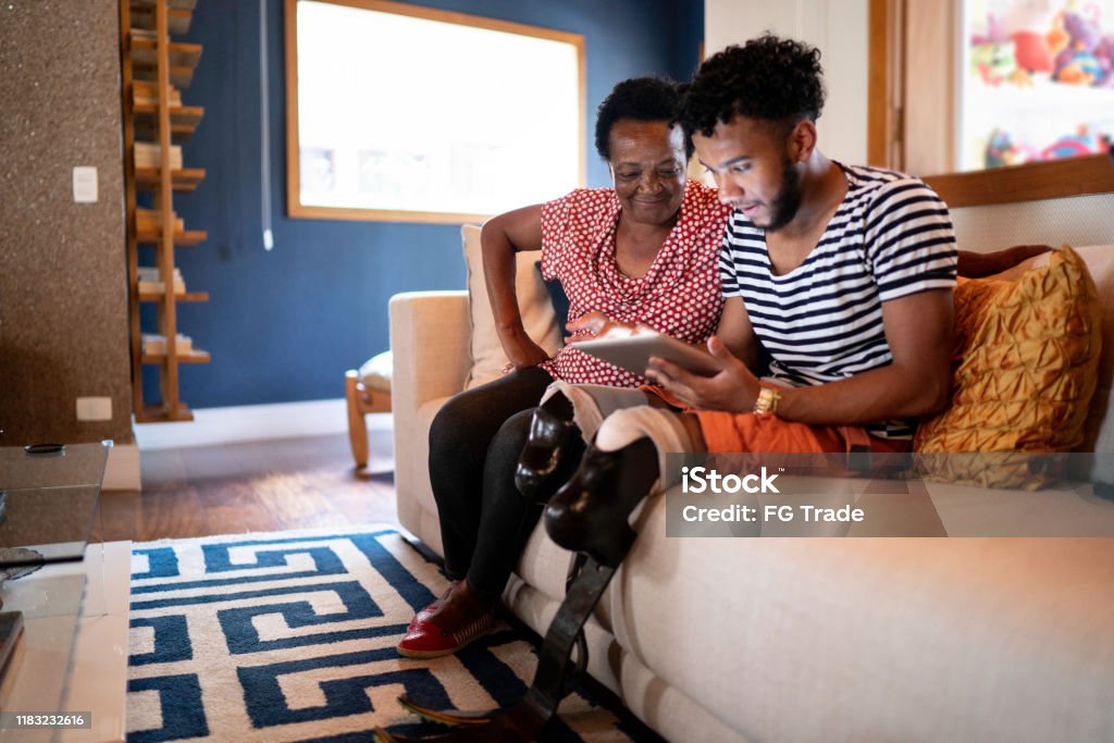 Son/Grandson using digital tablet with his mother/grandmother Disability Stock Photo