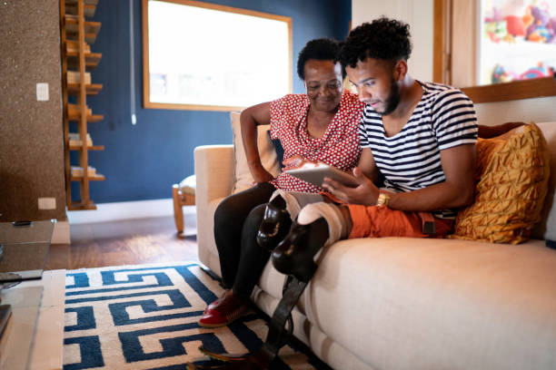 Son/Grandson using digital tablet with his mother/grandmother Son/Grandson using digital tablet with his mother/grandmother physical disability photos stock pictures, royalty-free photos & images