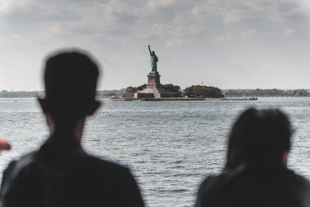 vista della statua della libertà tra due sagome di turisti - ferry new york city ellis island new york state foto e immagini stock