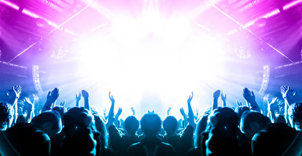 Concert crowd in front of a live stage Concert hall crowded with people in front of a stage lit for the gig. concert hall stock pictures, royalty-free photos & images