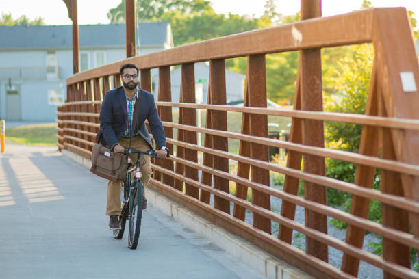 Biking To Work An attractive Indian businessman is bicycling to work. He is on a bridge on a sunny, summer day. He smiles widely as his suit jacket and bag blow in the wind. indian man walking in park stock pictures, royalty-free photos & images