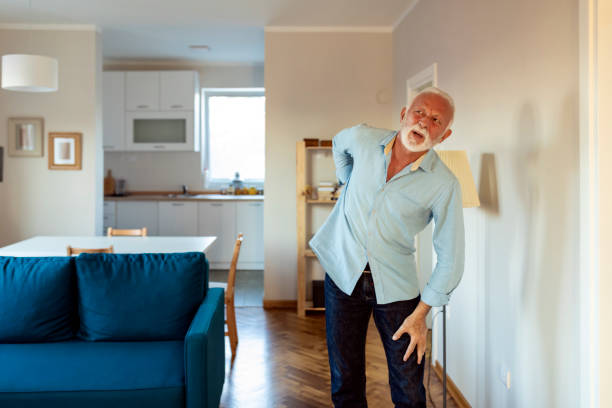 starszy mężczyzna w codziennym pokoju z bólem w plecach - backache lumbar vertebra human spine posture zdjęcia i obrazy z banku zdjęć