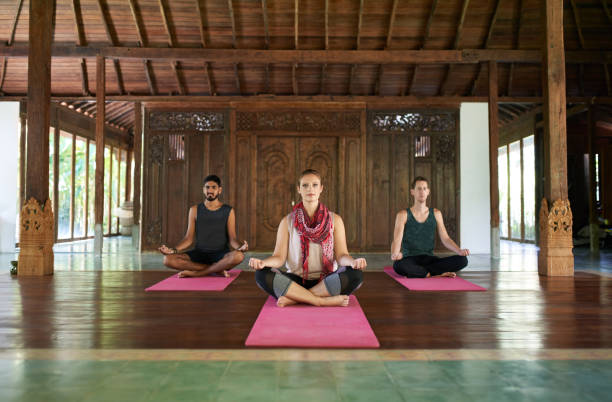 istock Three multi-ethnic people sitting in lotus pose practicing yoga together in a traditional temple in Bali Indonesia 1183254221