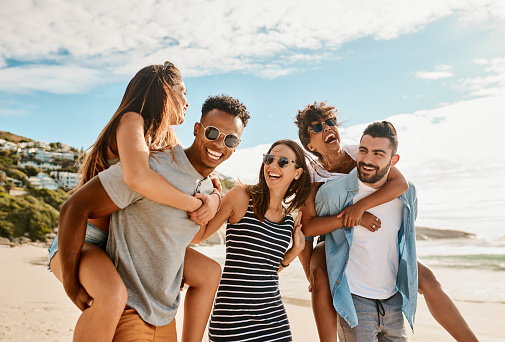 Shot of a group of happy young friends enjoying piggyback ride at the beach