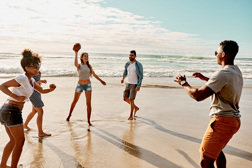 Shot of a group of happy young friends playing catch with a ball at the beach