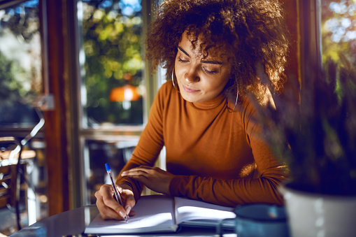 Retrato de lindo estudiante de carrera mixta con el pelo rizado y en cuello de tortuga sentado en el café y estudiando para los exámenes. photo
