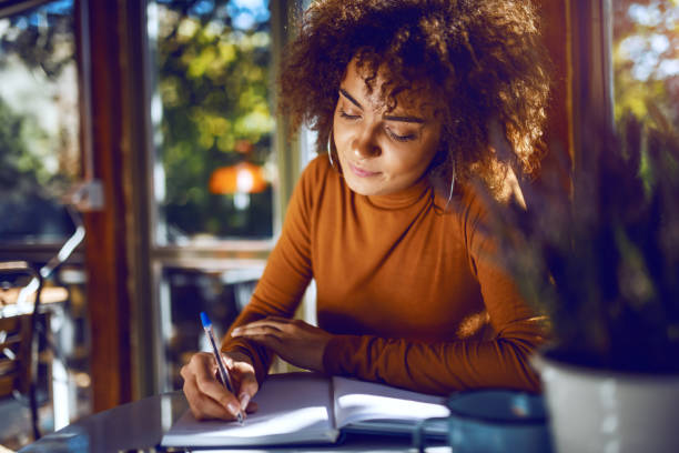 Portrait of cute mixed race student with curly hair and in turtleneck sitting in cafe and studying for exams. Portrait of cute mixed race student with curly hair and in turtleneck sitting in cafe and studying for exams. high collar stock pictures, royalty-free photos & images