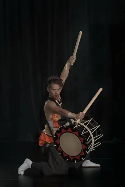 Photo of Full length portrait of a Japanese drummer Taiko on a dark stage.