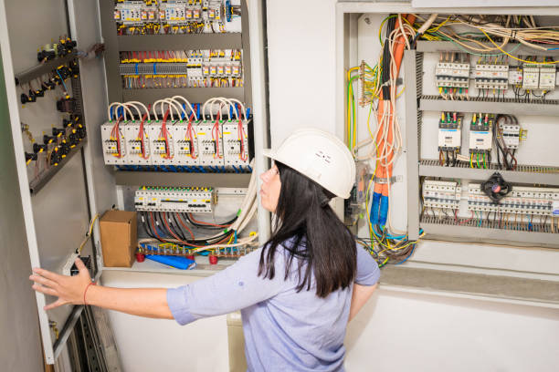istock The specialist works in the electrical distribution panel. Female engineer in white helmet switches on circuit breakers in electrical box. Professional girl checks the switchboard of the enterprise. 1183301847