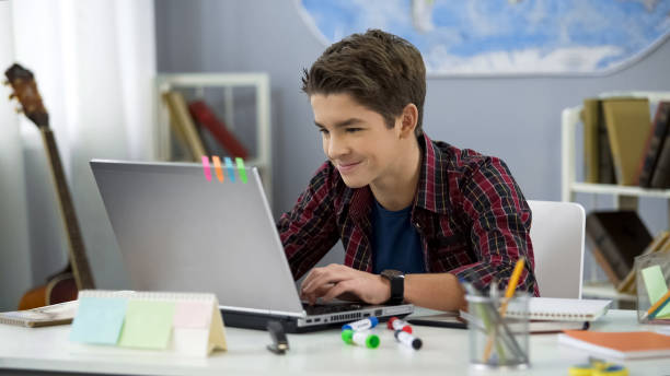 sonriendo adolescente hombre charlando con amigos en las redes sociales sentado sente portátil delantero - schoolboy fotografías e imágenes de stock