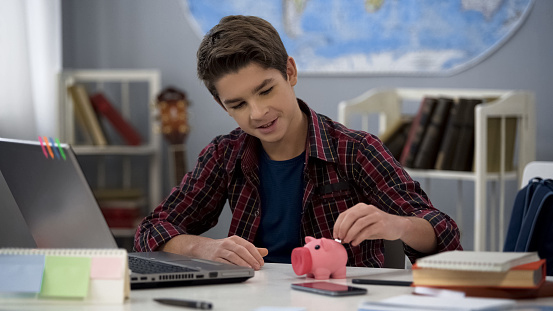 Niño masculino poniendo moneda en la alcancía, ahorrando dinero de bolsillo, finanzas photo