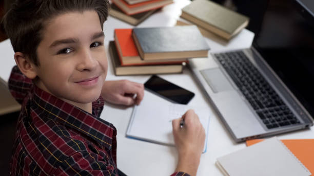 istock Male pupil smiling on camera doing homework sitting at table, gifted child 1183307413