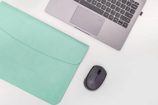 Top view of white working table with modern laptop, mint color leather case for personal computer and wireless mouse. Work space for school or office. Copy space. Flat lay.