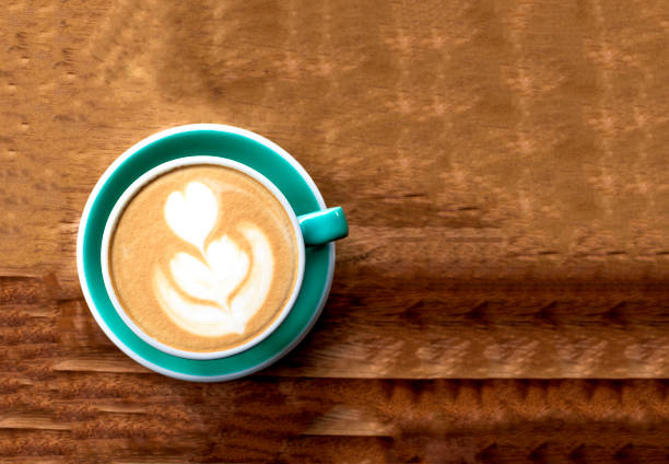 A cup of cappuccino with latte art on a wooden background. Beautiful foam, mint ceramic cup. Flat lay.