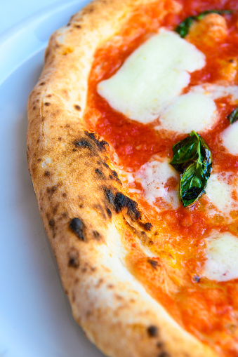 Close-up of the crust and topping of an original Neapolitan pizza with tomato sauce, buffalo mozzarella and slightly charred basil