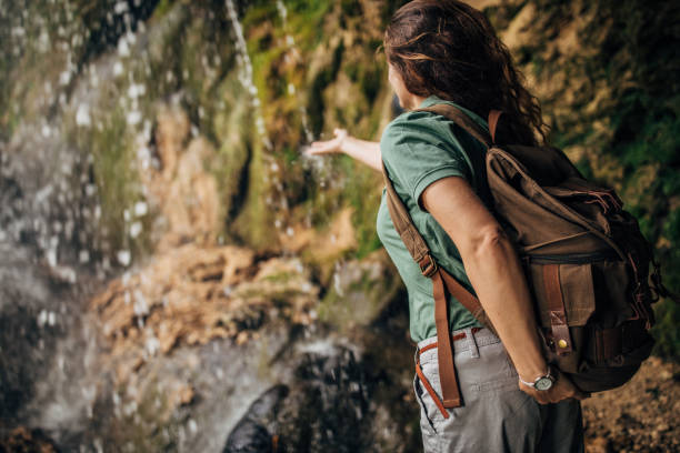 istock Woman with backpack by the waterfall in nature 1183313754