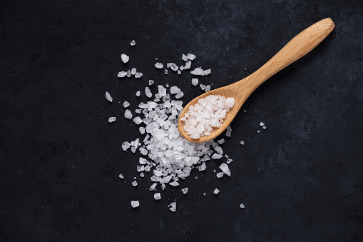 Heap of sea salt and a wooden spoon on dark background