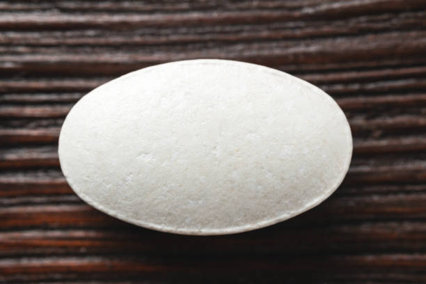 istock White medical supplement pill on wooden background, macro image, top view 1183316010