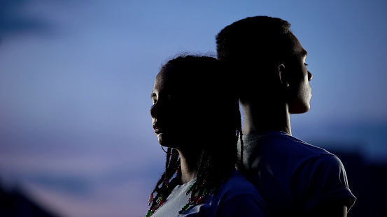 Couple standing to each other back in darkness, confronting problems together