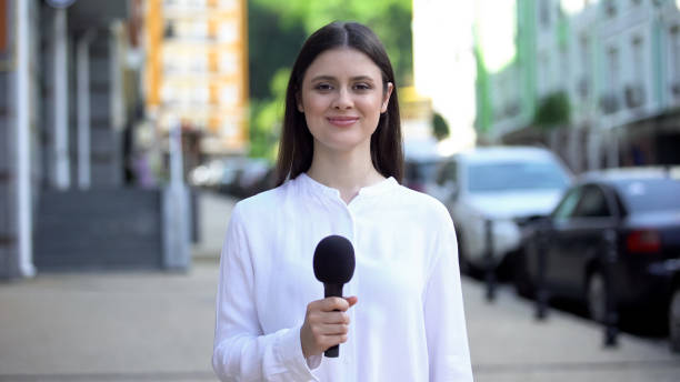 istock Cheerful female reporter holding microphone and smiling at camera, interview 1183325206