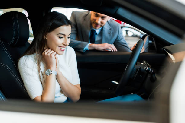 selective focus of smiling girl sitting in car near bearded man in car showroom selective focus of smiling girl sitting in car near bearded man in car showroom car ownership photos stock pictures, royalty-free photos & images