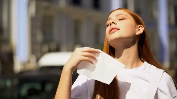 Young female teenager suffering city heat, waving napkin, trying to cool down