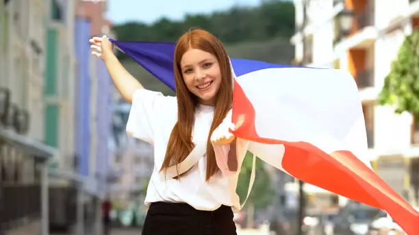 Joyful teen girl waving flag of France and smiling, patriotism and national fest