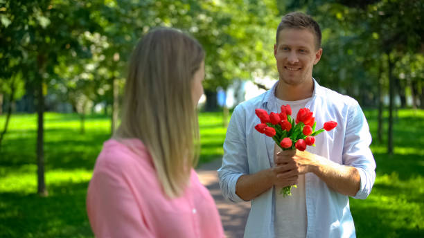 istock Smiling handsome man with red tulips looking girlfriend, romantic date present 1183326083