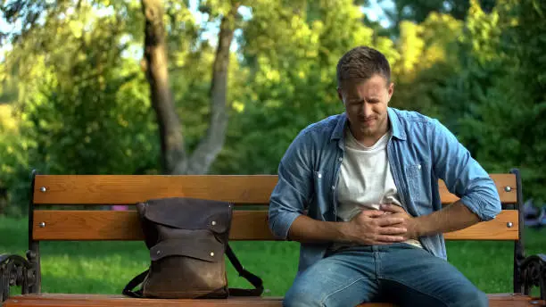 Photo of Man suffering stomach ache sitting bench, gastritis problem, food poisoning